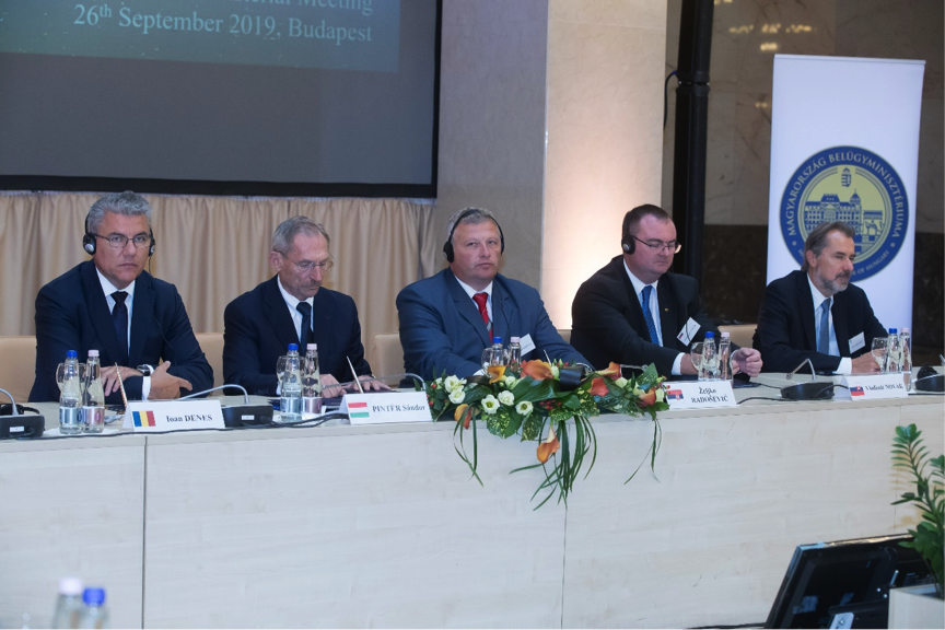 several men in business suits sitting at a table in front of a screen