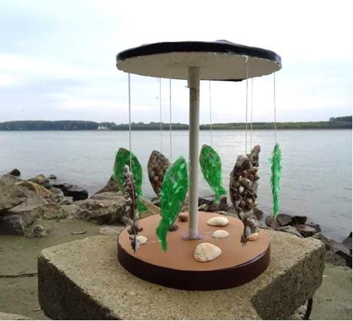 an artsy carousel with fish and shells next to a body of water