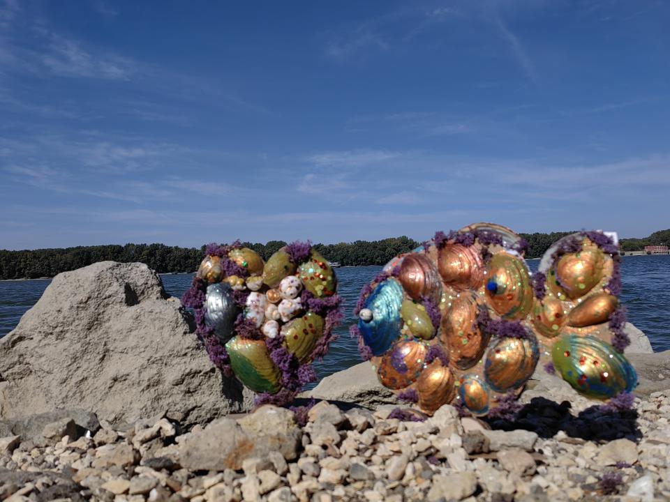 Shells painted in gold, green and blue, assembled in two sets and displayed on the shore of the Danube